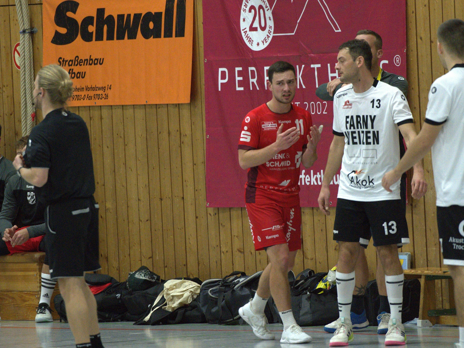 In der Sporthalle läuft ein Handballspieler des HRW-Laupheim in rotem Trikot an zwei Spielern des TV Altenstadt vorbei. Werbebanner und Sporttaschen sind im Hintergrund zu sehen.