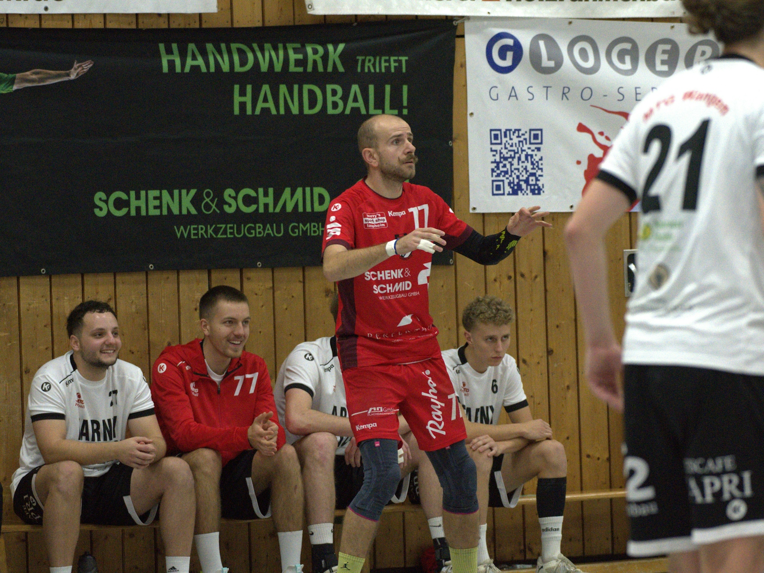 Im Fokus ist der Spieler mit der Trikotnummer 77 des HRW-Laupheim, dahinter sitzen vier Spieler des TV Altenstadt auf der Bank.